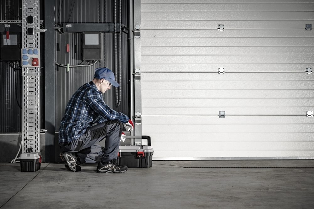 person kneeling while repairing a garage door